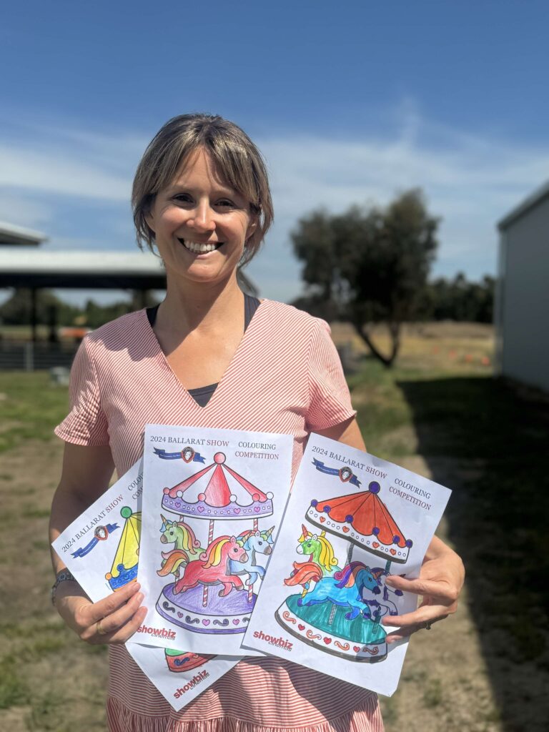 Smiling woman holding colouring competition entries outdoors.