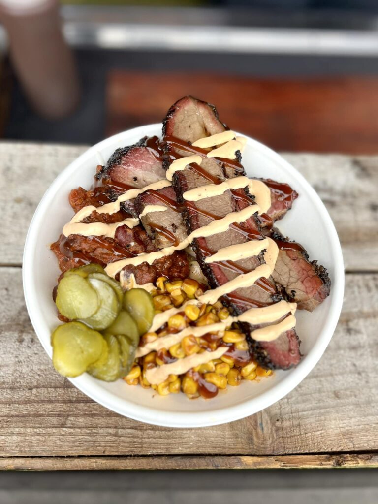 Brisket bowl with corn, pickles, and sauce.